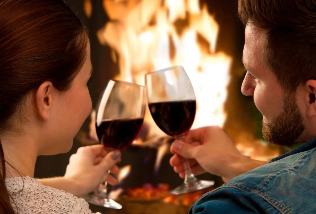 romantic couple enjoying red wine by the fire
