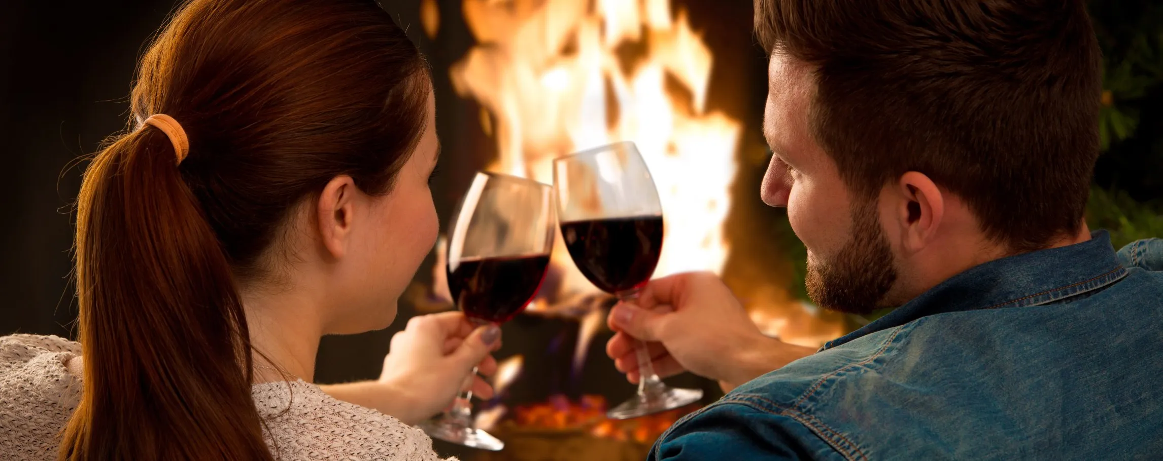 romantic couple enjoying red wine by the fire
