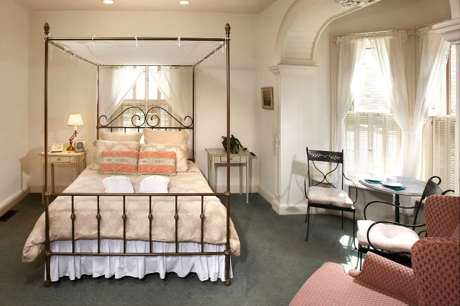 Carpeted room with queen bed in pink linens, with chairs and windows lining the room