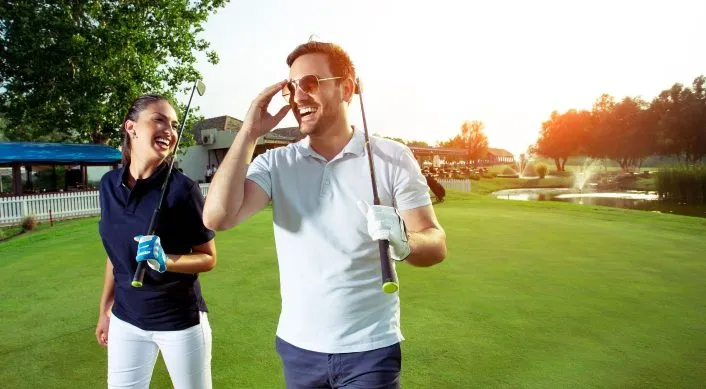 man and woman laughing and carrying golf clubs