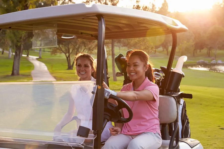 two women riding in a golf cart on a golf course