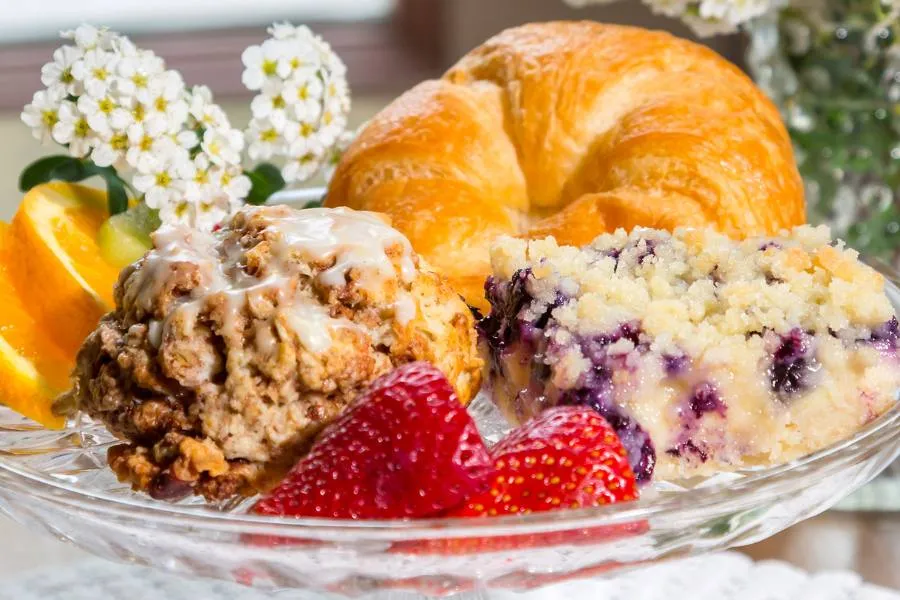 Selection of baked breakfast goods on a glass platter with fruit