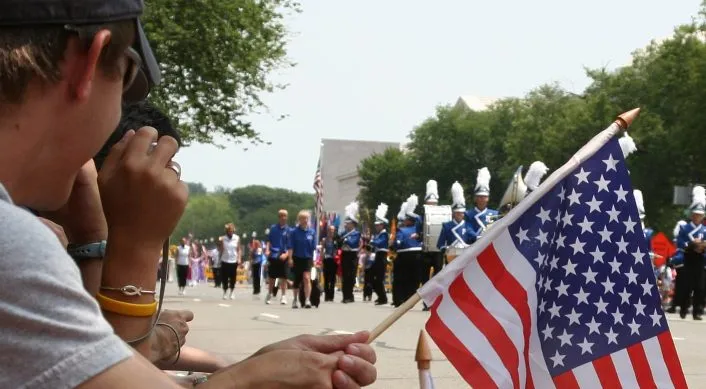 man holding American flag while watching parade